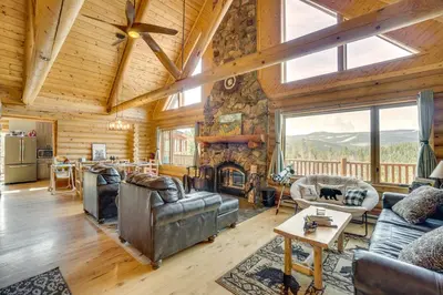 a living room with a stone fireplace in a log cabin at Mountain-View Front Range Colorado Vacation Rental in Red Feather Lakes