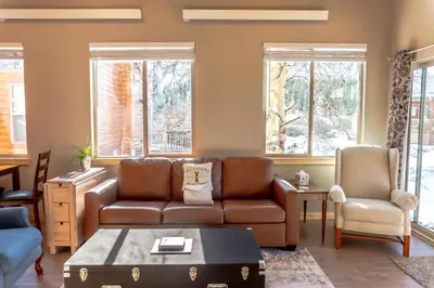 a living room with a brown couch and two windows at 2BR Riverside Chalet Near Trails in Breckenridge