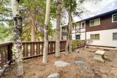 a house with a fence and trees in a yard at Riverfront Condo Near Downtown Estes Park! in Estes Park