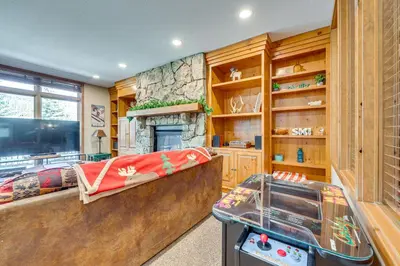 a living room with a stone fireplace and a game room at Walk to Gondola Condo with Deck in Winter Park! in Winter Park