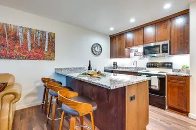 a kitchen with wooden cabinets and a counter with bar stools at Estes Park Condo Rental Balcony with River Views! in Estes Park