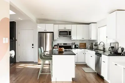 a kitchen with white cabinets and a stainless steel refrigerator at Chic Mid-Century Home Near Olde Town Arvada in Arvada