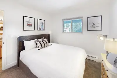 a bedroom with a bed with white sheets and two windows at Mountain Vista Retreat in Winter Park