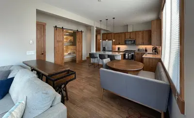 a living room with a couch and a table and a kitchen at Brand New! Private hot tub, bunk room and walkable to restaurants/shops in Fraser