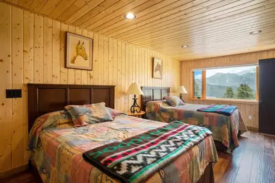 two beds in a room with wooden walls and a window at Frontier Mountain Retreat - Monthly Long-Term Vacation Rental 30 Days Minimum -- Estes Park apts in Estes Park