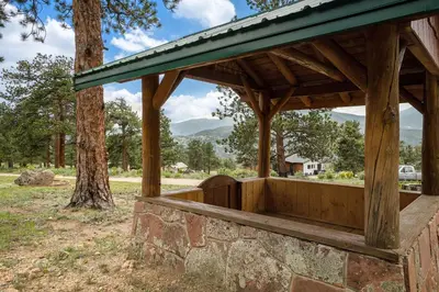 a wooden pavilion with a tree and mountains in the background at Frontier Mountain Retreat - Monthly Long-Term Vacation Rental 30 Days Minimum -- Estes Park apts in Estes Park