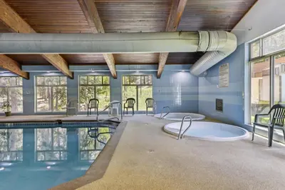 a swimming pool with two hot tubs in a room with windows at Cozy Winter Park Condo Bike, Ski, and Hike! in Winter Park