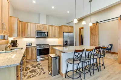 a kitchen with wooden cabinets and a island with bar stools at Mountain-View Fraser Condo with Balcony and Hot Tub! in Fraser