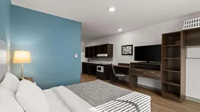 a bedroom with a bed and a desk with a television at WoodSpring Suites Greeley in Greeley