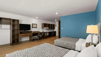 a room with two beds and a desk with a television at WoodSpring Suites Greeley in Greeley