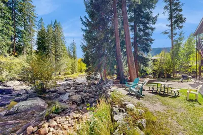 a backyard with two picnic tables and a creek at On the Rapids - A Unit in Grand Lake