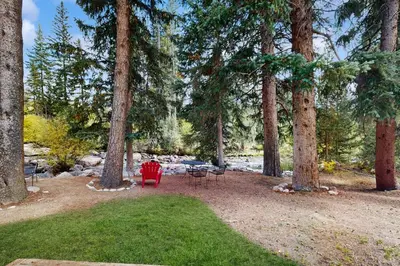 a yard with a red chair and tables and trees at On the Rapids - B Unit in Grand Lake