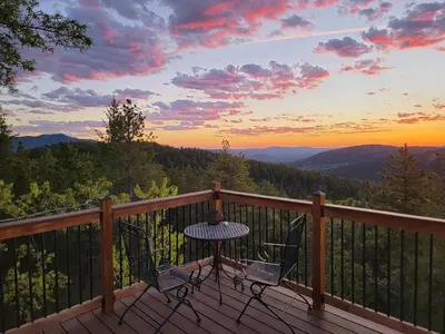 a table and chairs on a wooden deck with a sunset at The Tree House in Evergreen