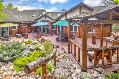 a house with a wooden deck with chairs and umbrellas at Aspen Suite - Hot Tub, Minutes to RMNP, Walking Distance to Mary's Lake in Estes Park