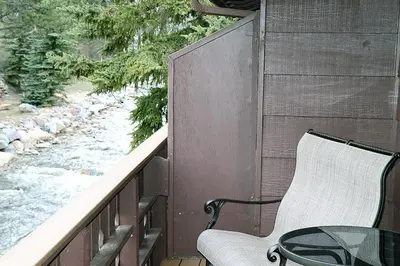 a balcony with a chair and a table and a river at Fawn Valley Inn- 210 condo in Estes Park