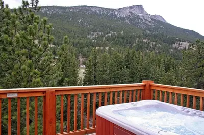 a hot tub on a wooden deck with a mountain at Fawn Valley Inn- 306 apts in Estes Park