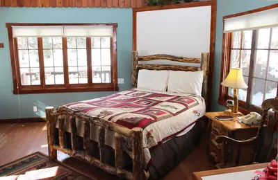 a bedroom with a bed and a table and windows at Fawn Valley Inn- 157 cabin in Estes Park