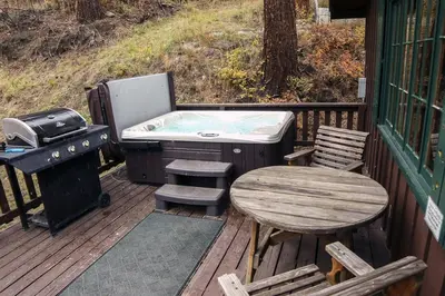 a hot tub and a table and a grill on a deck at Fawn Valley Inn- 157 cabin in Estes Park