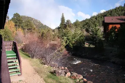 a bench next to a river next to a cabin at Fawn Valley Inn- 205 condo in Estes Park