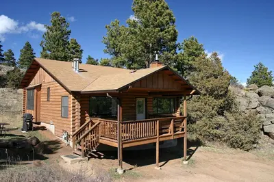 a log cabin with a large deck in the woods at Lazy R Cottages- 14 cabin in Estes Park