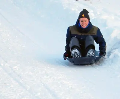 a person riding a sled down a snow covered slope at Red-tail Roundhouse at 22 West Cabins and Recreation in Hebron