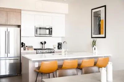 a kitchen with a white counter and orange chairs at Skytop Perspective | Espadin LoHi in Denver