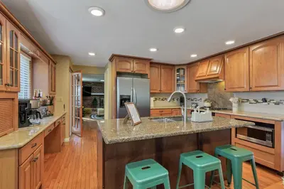 a kitchen with wooden cabinets and green stools at ᨒFIREHAUSᨒHotTubᨒCinemaᨒBBQᨒBadmintonᨒGames in Arvada