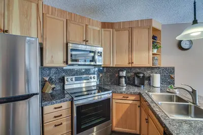 a kitchen with wooden cabinets and stainless steel appliances at Ski-InandSki-Out Winter Park Condo with Mountain Views in Winter Park