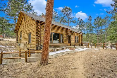 a log cabin in the woods next to a tree at Hidden Pines -- EV#3034 home in Estes Park