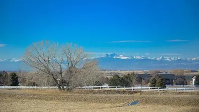 a tree in a field with a fence and mountains at Luxury Home with Spectacular Rocky Mountain Views! in Eaton