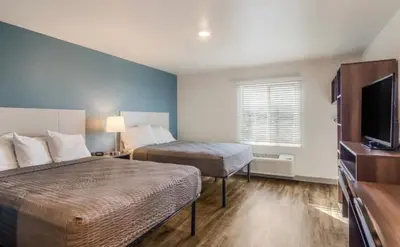 a hotel room with two beds and a flat screen tv at WoodSpring Suites Denver Commerce City in Commerce City