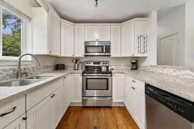 a kitchen with white cabinets and a stove and a sink at Sherwood Cottage - Steps from Old Town & Poudre River in Fort Collins