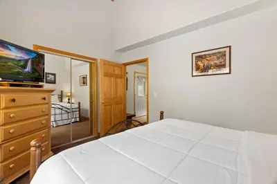 a bedroom with a white bed and a dresser with a television at Creekside Suites 10 by Estes Park Condos in Estes Park