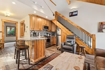 a kitchen and living room with wooden cabinets and a staircase at Creekside Suites 21 by Estes Park Condos in Estes Park