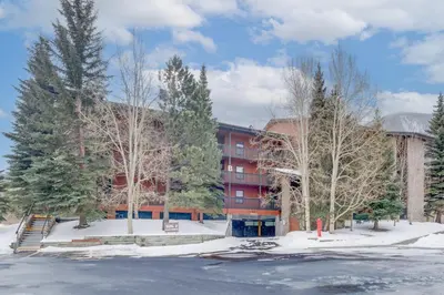 a building in a parking lot with trees and snow at Mountainside B173 by Great Western Lodging in Frisco