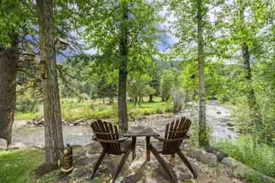 a table and two chairs sitting next to a river at Elk River Cabin -- Cabin Condo in Estes Park -- 23-ZONE3554 condo in Estes Park