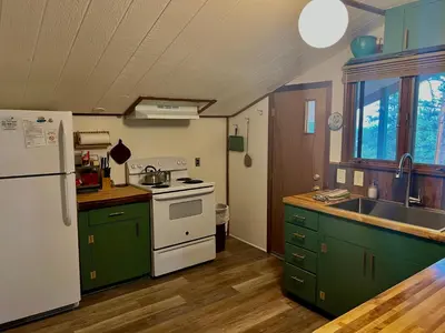 a kitchen with green cabinets and a white refrigerator at Rose Den - Romantic Mountain Cabin with Views! in Estes Park