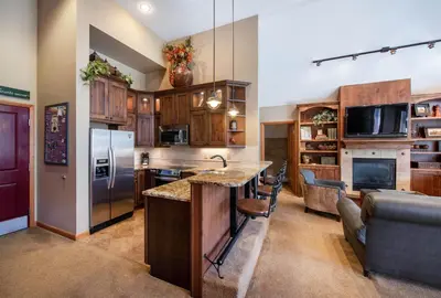 a kitchen with wooden cabinets and a bar with a couch at Select Unit 1710 - 2BR - Zephyr Mountain Lodge condo in Winter Park