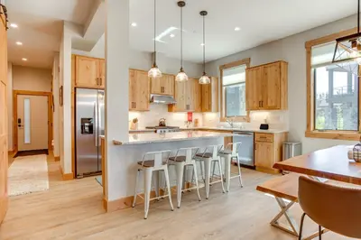 a kitchen with wooden cabinets and a bar with stools at Modern Condo with Hot Tub 5 Mi to Winter Park! in Fraser