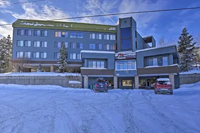 two trucks parked in front of a building in the snow at Walk to Dtwn Winter Park Studio with Hot Tub Access in Winter Park