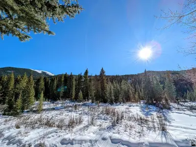 a snow covered field with trees and the sun in the sky at Mill Creek 201 by SummitCove Lodging in Keystone