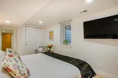 a bedroom with a large white bed and a flat screen tv at Steps from Wash Park Modern Apt, Patio and Parking in Denver