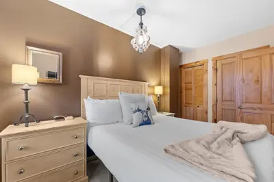 a bedroom with a white bed with a dresser and a lamp at Buffalo Lodge 8386 in Keystone