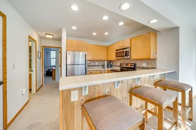 a kitchen with wooden cabinets and a counter with stools at 2 Mi to Winter Park Resort Condo with Pool Access! in Winter Park