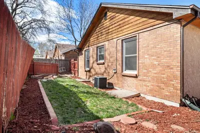 a brick house with a yard next to a fence at A Denver Oasis 15 Min to the Bronco Stadium 3 Bedroom with a King Suite in Denver
