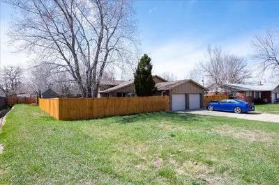 a house with a fence and a blue car in a yard at Modern Chic Retreat Near Mtns & Red Rocks Wifi in Wheat Ridge