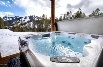 a jacuzzi tub in the snow with mountains in the background at Antler at Lakota 407 home in Winter Park