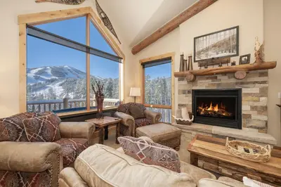 a living room with a fireplace with a mountain view at Antler at Lakota 407 home in Winter Park