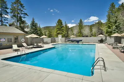 a large swimming pool with chairs and umbrellas at Flying Dutchman Mountainside Condo: Pool/Hot Tub in Keystone
