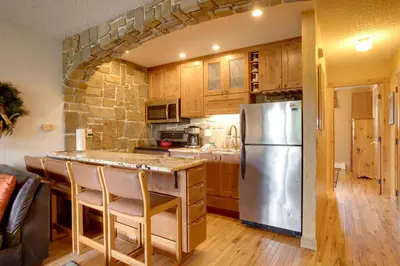 a kitchen with a stainless steel refrigerator and wooden cabinets at Pool and 3 Hot Tubs Winter Park Condo on Bus Line in Winter Park